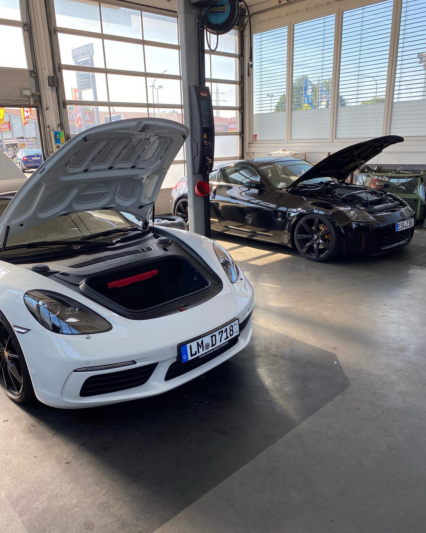 White Porsche 718 frunk open and black Nissan 350Z engine bay open in Unlimited Auto workshop Weiden.
