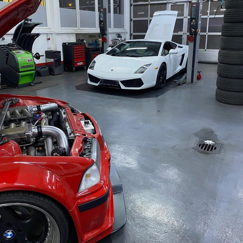 Inside Unlimited Auto workshop: a custom BiTurbo V12 BMW E36 and a white Lamborghini Gallardo on a lift.